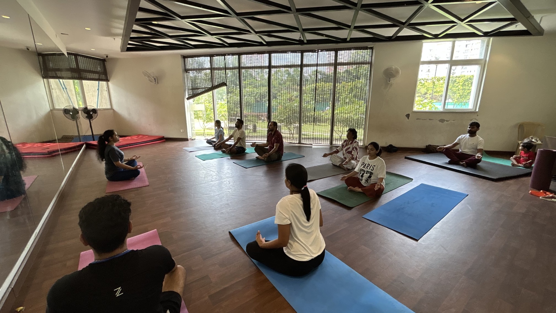 Students in padmasana meditation with garden view behind